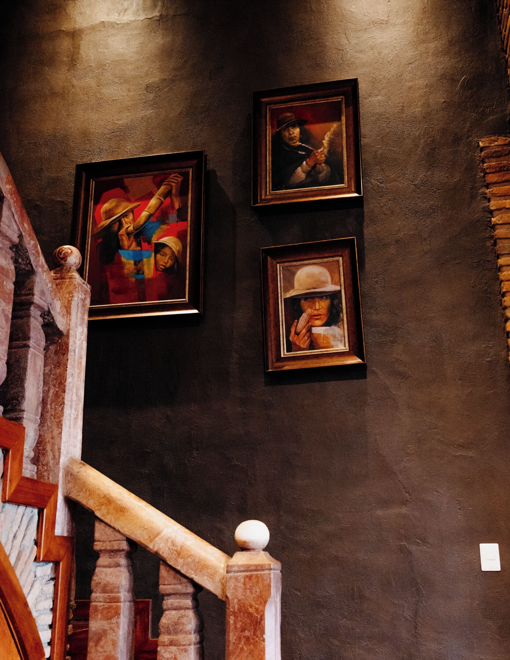 A staircase with a wooden handrail and a wall with three framed artworks.