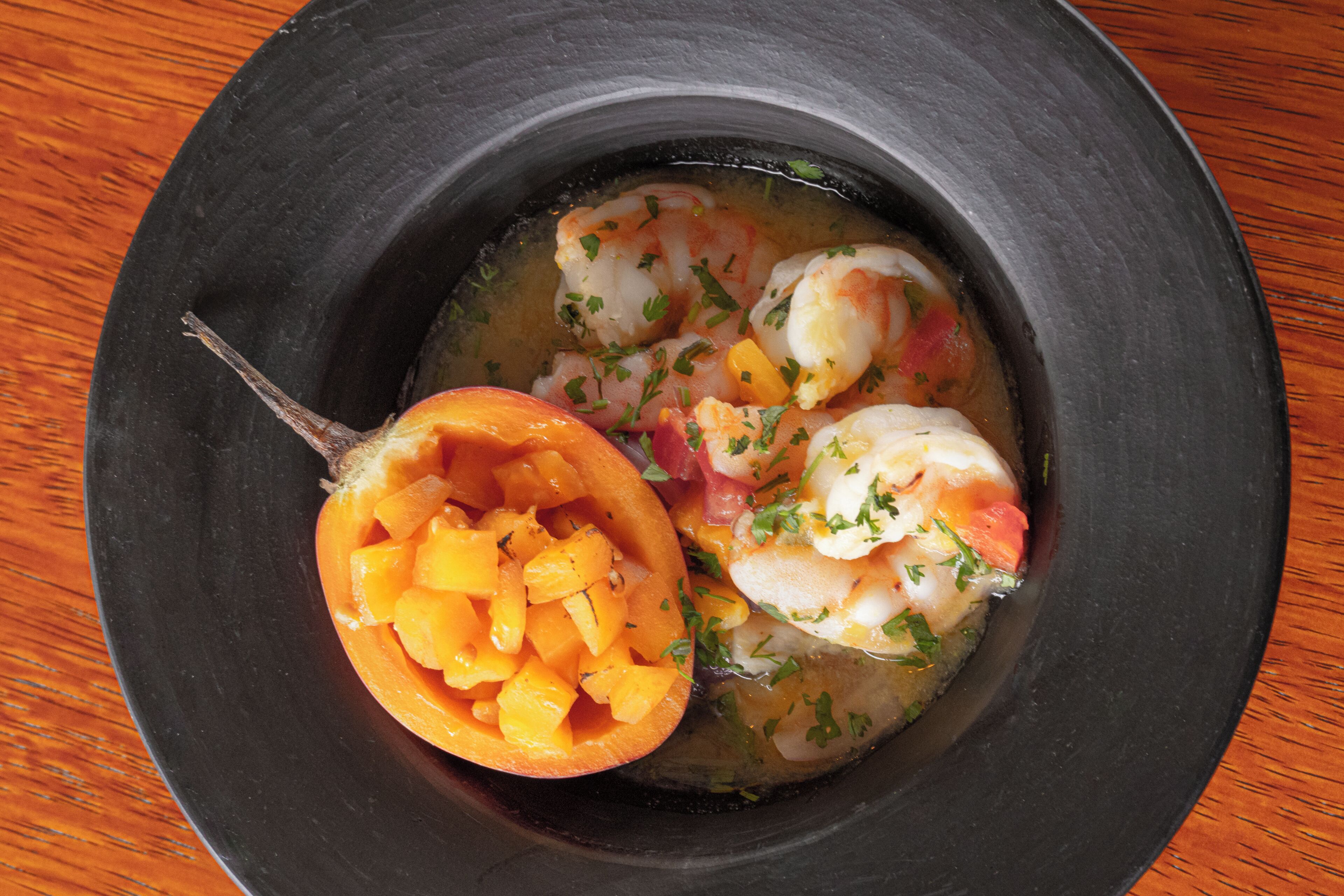 Un tazón de sopa de mariscos con camarones y una naranja cortada por la mitad.