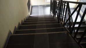 Una escalera con barandillas negras y escalones de baldosas oscuras.