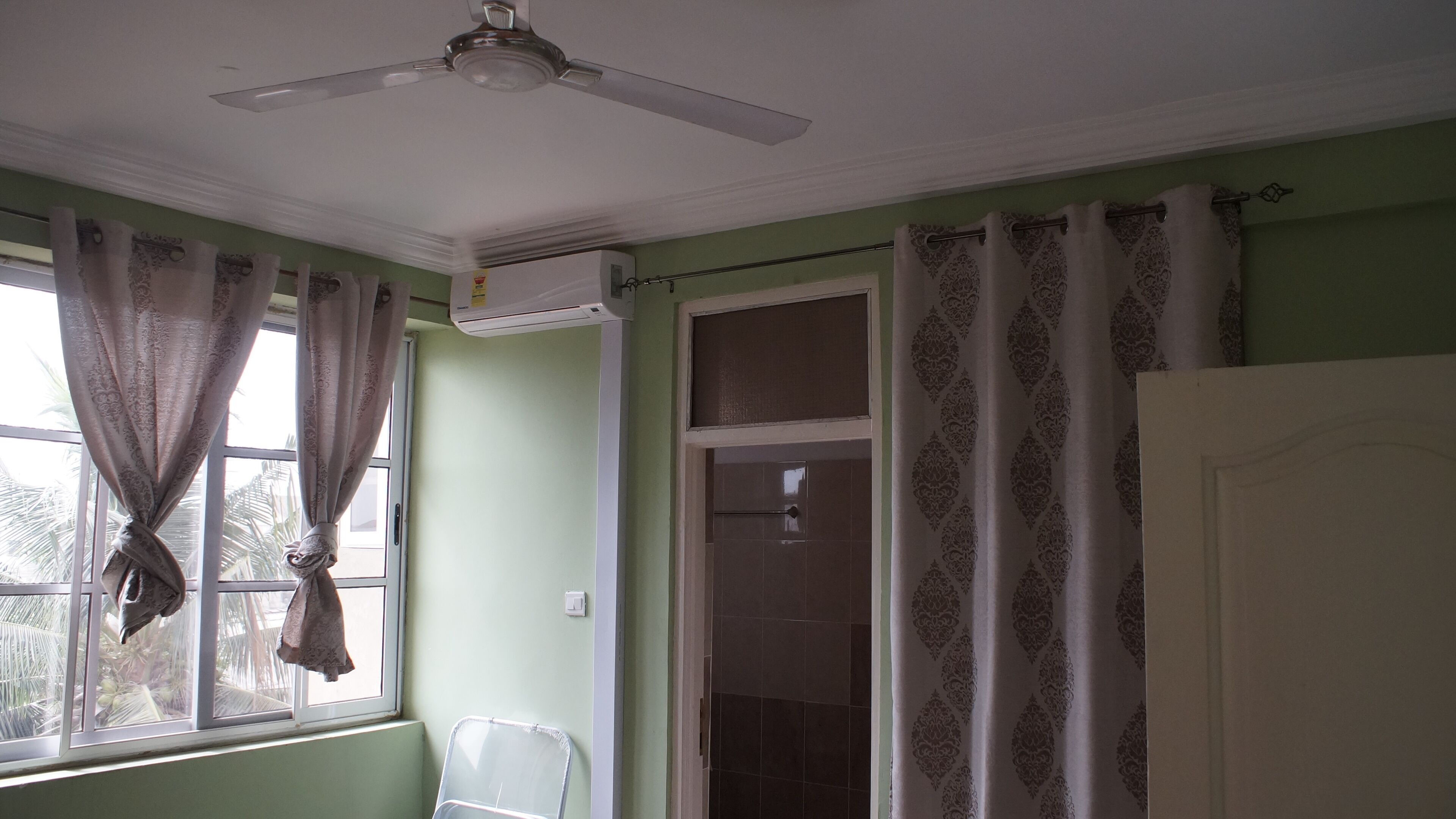 A bathroom with a ceiling fan, a window with curtains, a shower area, and a door.