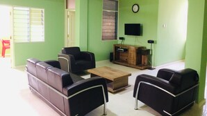 Una sala de estar con paredes verdes, un ventilador de techo, una mesa de centro de madera y sofás de cuero negro.