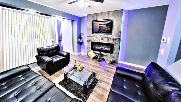 A modern living room with black leather sofas, a glass coffee table, a ceiling fan, a fireplace, and a TV mounted on the wall. - The Modern Spot (Winnipeg)