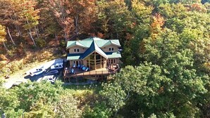 A large, two-story lodge with a prominent porch and a covered deck, surrounded by dense forest. - Panoramic Long Range Mountain Views on 4ac, Hot Tub, Pool Table, Arcade, Firepit (West Jefferson)