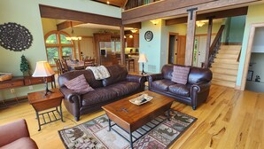 A spacious living room with leather sofas, a wooden coffee table, and a dining area with a chandelier. - Panoramic Long Range Mountain Views on 4ac, Hot Tub, Pool Table, Arcade, Firepit (West Jefferson)