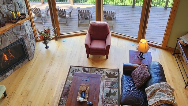 A cozy living room with a stone fireplace, leather sofas, and a large window offering a view of a forested mountain. - Panoramic Long Range Mountain Views on 4ac, Hot Tub, Pool Table, Arcade, Firepit (West Jefferson)