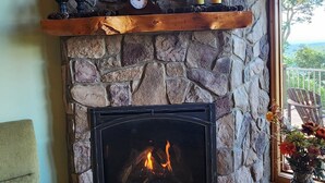 A stone fireplace with a mantel shelf, a green armchair, and a wooden floor. - Panoramic Long Range Mountain Views on 4ac, Hot Tub, Pool Table, Arcade, Firepit (West Jefferson)