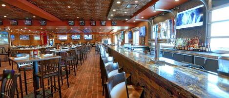 A restaurant with a long counter, multiple TVs, and a bar area with bottles.