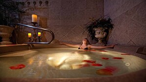A person relaxing in a hot tub with rose petals floating on the water, surrounded by decorative elements and a tiled wall. - STUNNING 2 BEDROOM AT LAKES RESORT NEAR DISNEY UNIVERSAL SEA WORLD (Orlando)