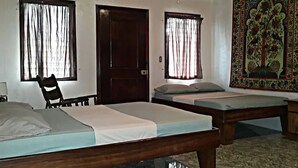 Quarto com duas camas de solteiro, uma escrivaninha de madeira, uma cadeira e uma porta.