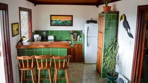 Uma cozinha com azulejos verdes, cadeiras de madeira, uma geladeira e um quadro na parede.