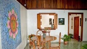 Uma sala de jantar com uma mesa redonda de madeira e cadeiras, uma grande peça decorativa na parede e um espelho sobre a mesa.
