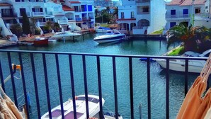 A balcony with a view of a marina, boats, and buildings with red-tiled roofs. - Beautiful T2 renovated, with bikes, on the water, beach on foot, full center. (Empuriabrava)