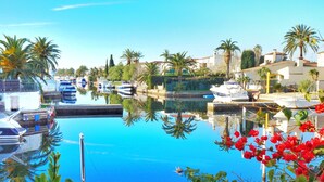 A marina with boats docked, a clear blue sky, and palm trees. - Beautiful T2 renovated, with bikes, on the water, beach on foot, full center. (Empuriabrava)