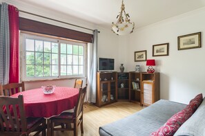 A room with a dining table, chairs, a sofa, a television, and a cabinet with decorative items.