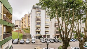 Un edifici residencial de diversos pisos amb balcons, un aparcament i un arbre al primer pla.
