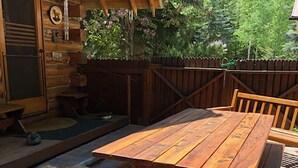 Een houten terras met een picknicktafel en banken, een hond die op de grond ligt, en een houten chalet in de verte.