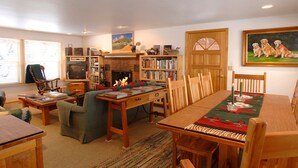 Een gezellige woonkamer met een open haard, boekenkasten, een eettafel met stoelen en een televisie.
