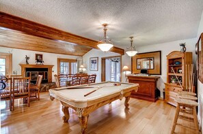 Relax in this spacious room featuring a pool table, fireplace, and high ceiling with exposed beams.