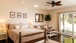 A bedroom with a large bed, bedside tables, a ceiling fan, a mirror, and a view of the outdoors through a sliding glass door.