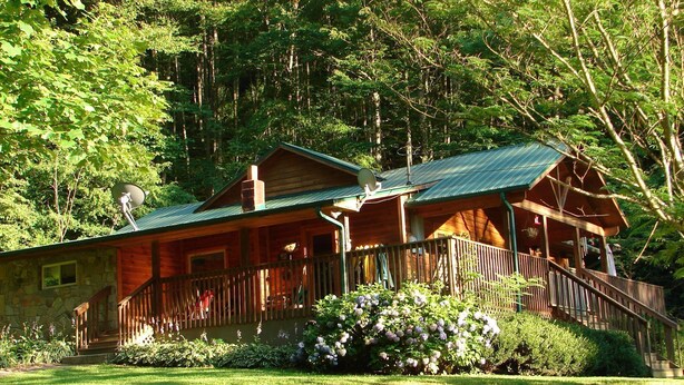 Eine Holzhütte mit Veranda, umgeben von üppigem Grün und Bäumen.