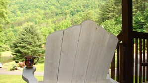 Ein Adirondack-Stuhl aus Holz mit einer Tasse, mit Blick auf einen üppigen grünen Wald und einen See.