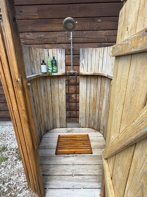 Eine Holzsauna mit einer Sitzbank, einer Duschbrause und Flaschen mit Shampoo und Conditioner auf einem Regal.