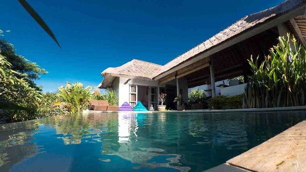 Une piscine d’eau bleue et limpide, avec une maison en arrière-plan.