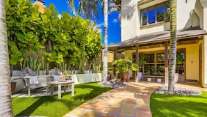 A patio with a tiled walkway, outdoor furniture, and lush greenery. - Tranquility La Jolla | Custom Home w/ Rooftop (San Diego)