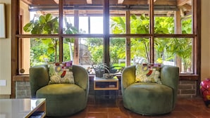 A room with two green armchairs, a small table, and a large window with a view of greenery. - Tranquility La Jolla | Custom Home w/ Rooftop (San Diego)