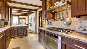 A spacious kitchen with wooden cabinets, a central island, stainless steel appliances, and a tiled backsplash. - Tranquility La Jolla | Custom Home w/ Rooftop (San Diego)