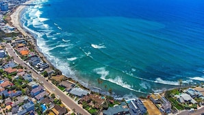 An aerial view of a coastal residential area with houses along the beachfront, a pier extending into the ocean, and a clear sky. - Tranquility La Jolla | Custom Home w/ Rooftop (San Diego)