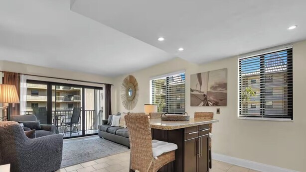 A modern living room with a sofa, a wicker chair, a kitchen island, and a dining area with a table and chairs. - Walk to Beach & Rooftop Pool by Luxury Resorts (Naples)