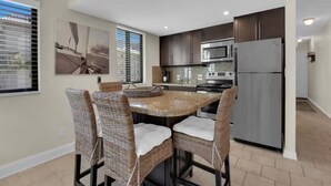 A modern kitchen with a central island, dark cabinetry, stainless steel appliances, and wicker chairs. - Walk to Beach & Rooftop Pool by Luxury Resorts (Naples)