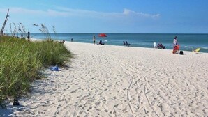 A sandy beach with footprints, a red umbrella, and people in the distance. - Walk to Beach & Rooftop Pool by Luxury Resorts (Naples)
