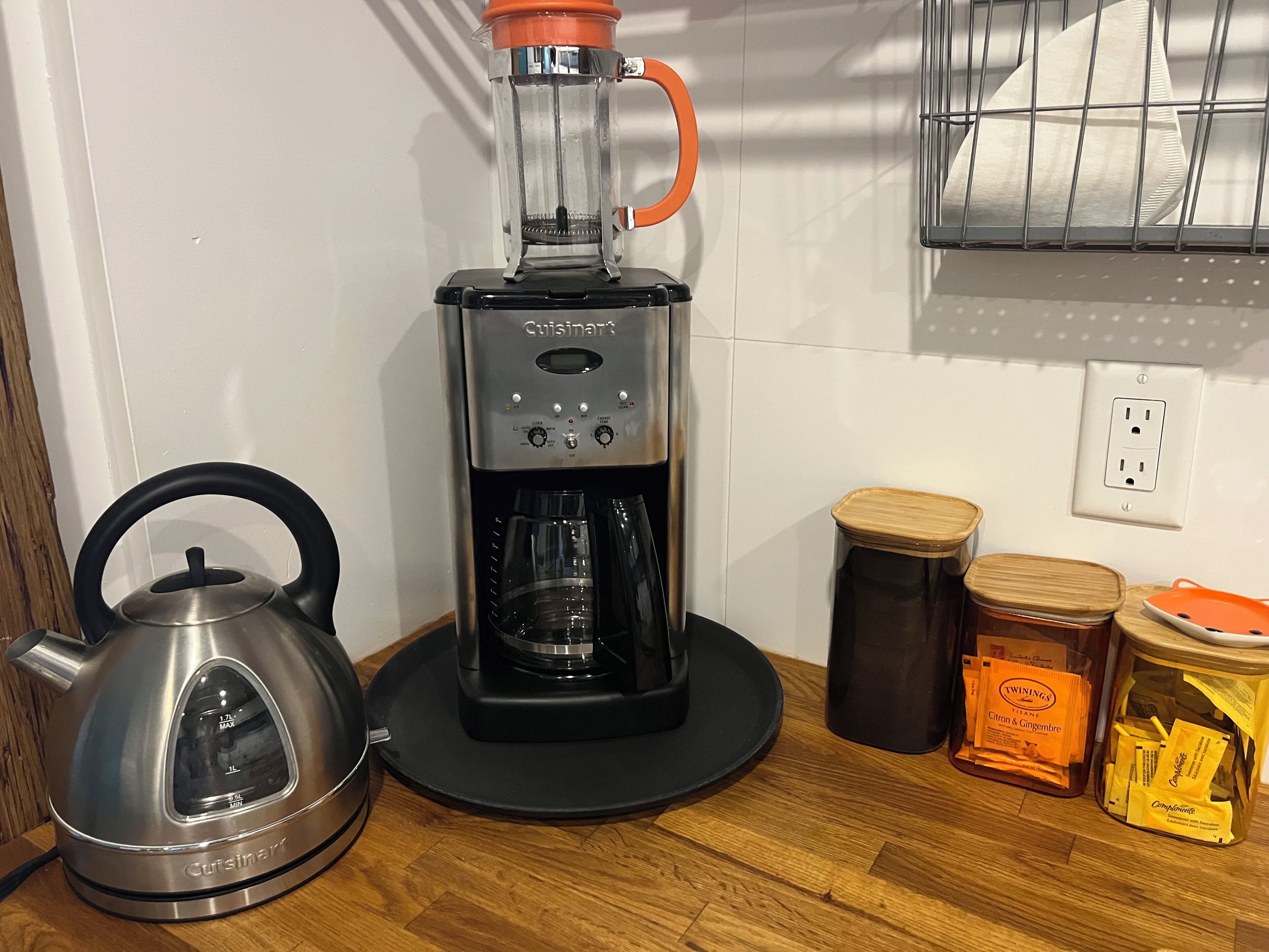 A kitchen with a Cuisinart coffee maker, a kettle, and containers of Twinings tea and other tea bags.