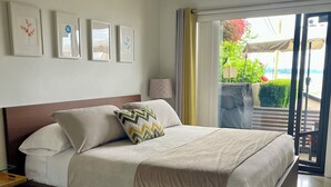 Ein modernes Schlafzimmer mit einem großen Bett, einem Nachttisch, einer Lampe und Blick ins Freie durch eine Schiebetür.
