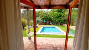 Vista a través de un vidrio hacia un patio trasero con piscina, patio de ladrillo y una pérgola de madera.