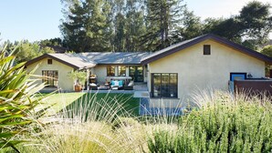 Una casa moderna con un patio, mobiliario exterior y un amplio ventanal con vistas a un jardín.