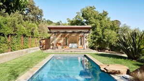 Una piscina rectangular con borde de piedra, rodeada por un césped cuidado y una zona de patio con mobiliario exterior.