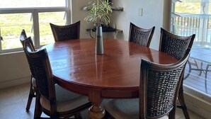 Een eethoek met een ronde houten tafel, omringd door rieten stoelen, een potplant en decoratieve objecten op planken.