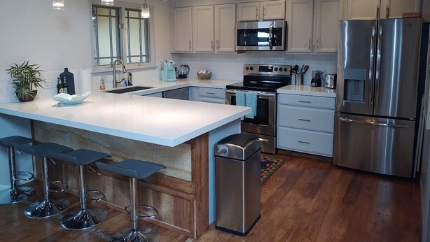 A modern kitchen with stainless steel appliances, a large island with bar stools, and a view of the living area.