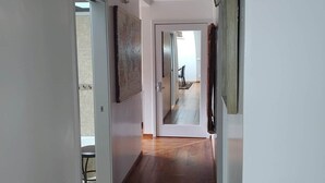 A hallway with wooden flooring, white walls, and a door leading to another room.