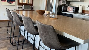Eine moderne Küche mit einer großen Kochinsel, Barhocker, einem Kühlschrank, einer Mikrowelle und einem Essbereich mit großem Fenster.