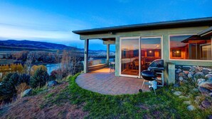 Ein modernes Haus mit Terrasse, Grill und Blick auf die Landschaft.