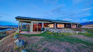 Ein modernes Haus mit einer großen Terrasse, einem überdachten Sitzbereich im Freien und Blick auf die umliegende Landschaft.