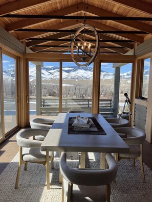 A dining area with a table and chairs, large windows with a mountain view, and a wooden ceiling. - Riverfront property with the best views in Paradise valley! (Livingston)