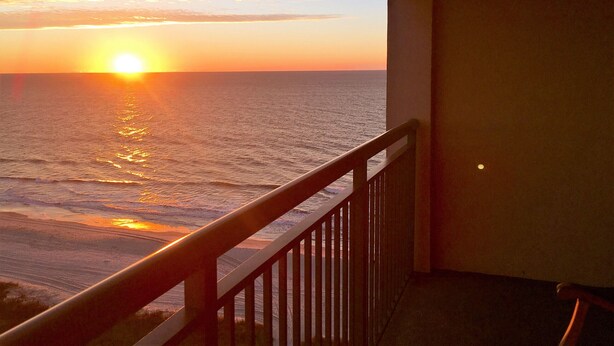 Un balcon avec vue sur l’océan au coucher du soleil.