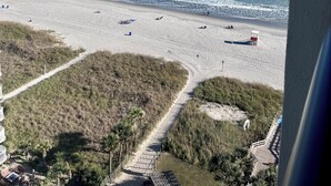 Une vue sur la plage, avec un ciel dégagé, une plage de sable et une promenade en bois menant à un bâtiment doté d’une terrasse.