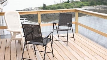Une terrasse en bois avec deux chaises, une blanche et une noire, donnant sur une étendue d’eau bordée d’une rive rocheuse et avec des arbres en arrière-plan.