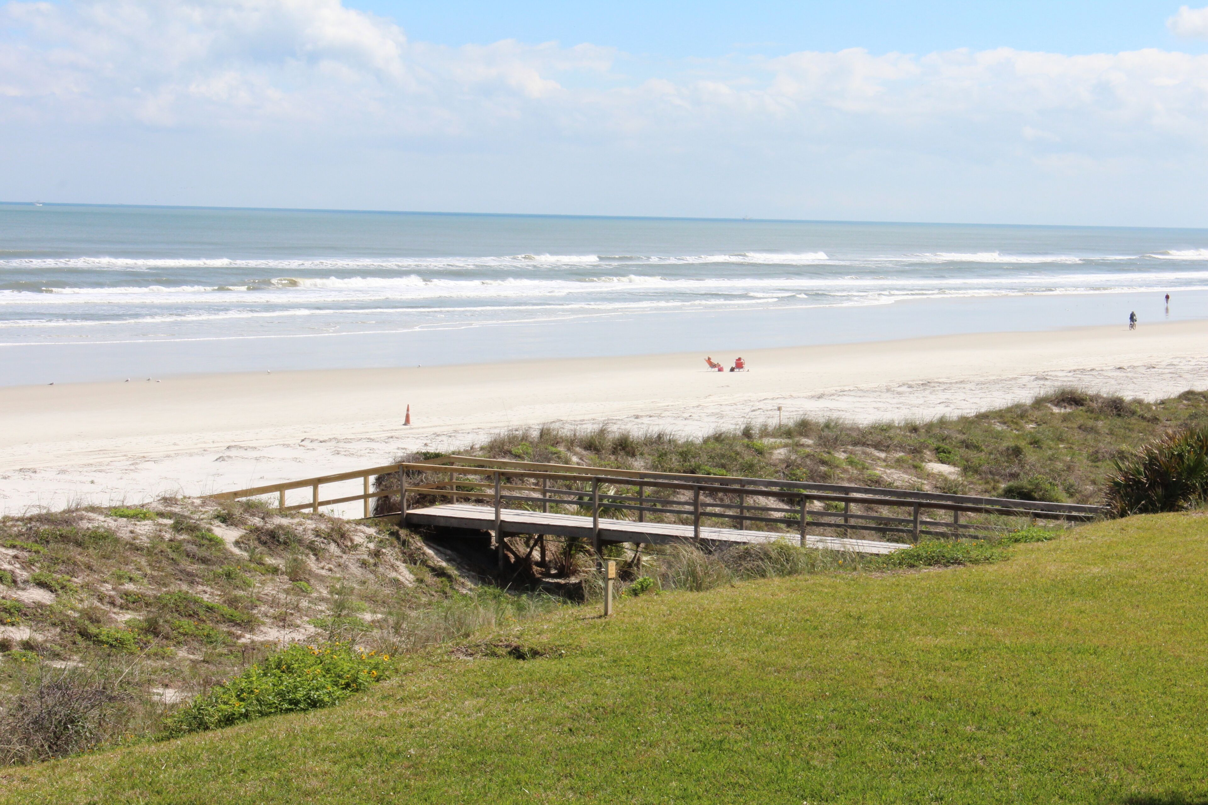 Une plage avec un pont en bois, un rivage sablonneux et une vue sur l’océan.